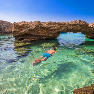 Blue Lagoon, Malta - Snorkeling tourist at the caves of the Blue Lagoon on the island of Comino on a bright sunny summer day with blue sky